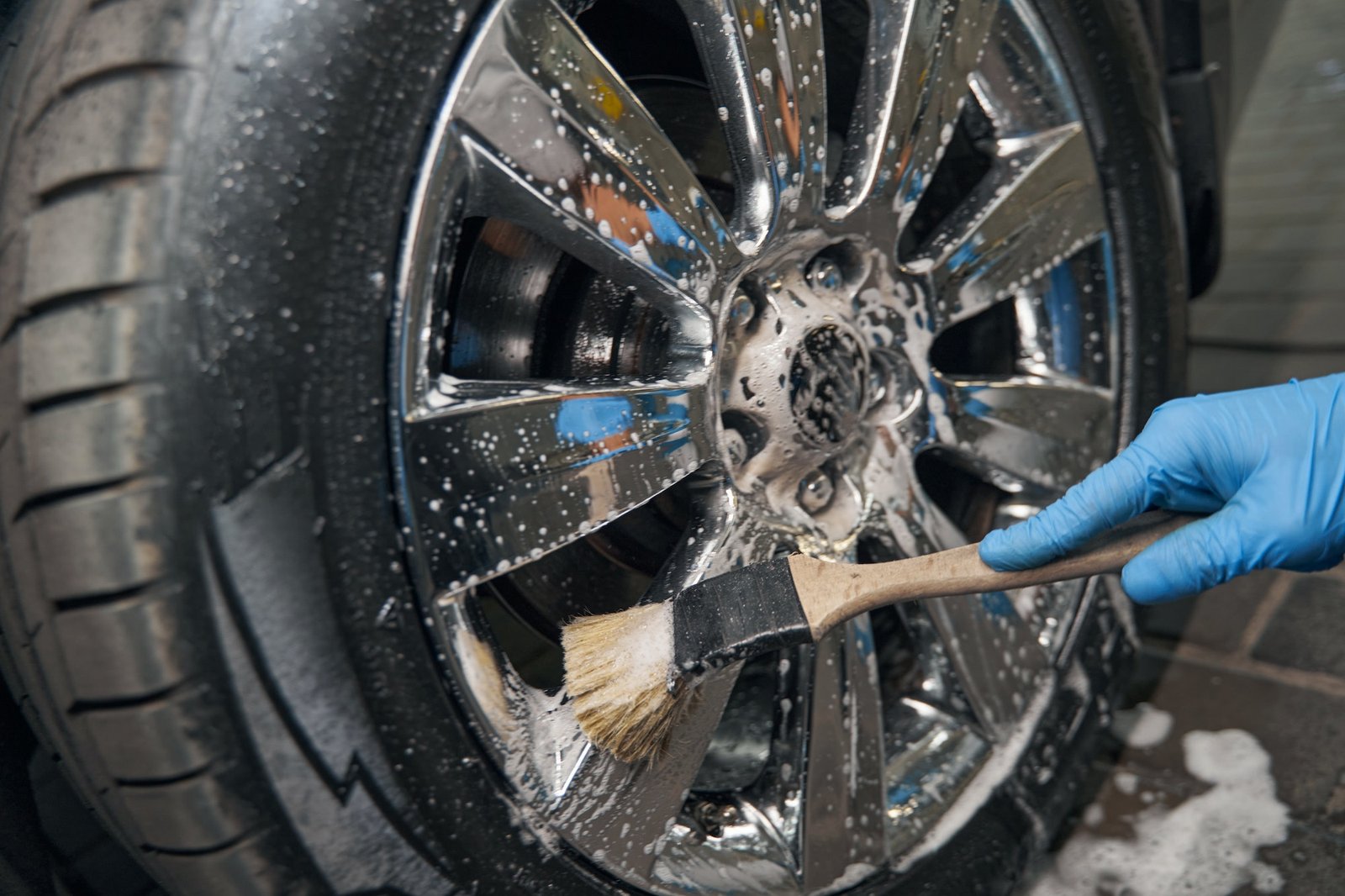 Car detailing studio worker cleaning car wheel with brush